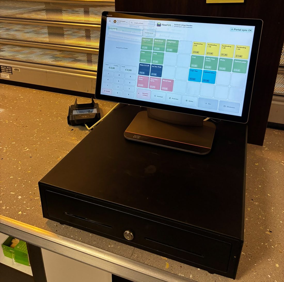 De kantinekassa van het Kalsbeek College, locatie Schilderspark: een Sunmi D3 op een kassalade, met broodjes, soep, fruit en drinken als gekleurde knoppen en een pinautomaat ernaast.